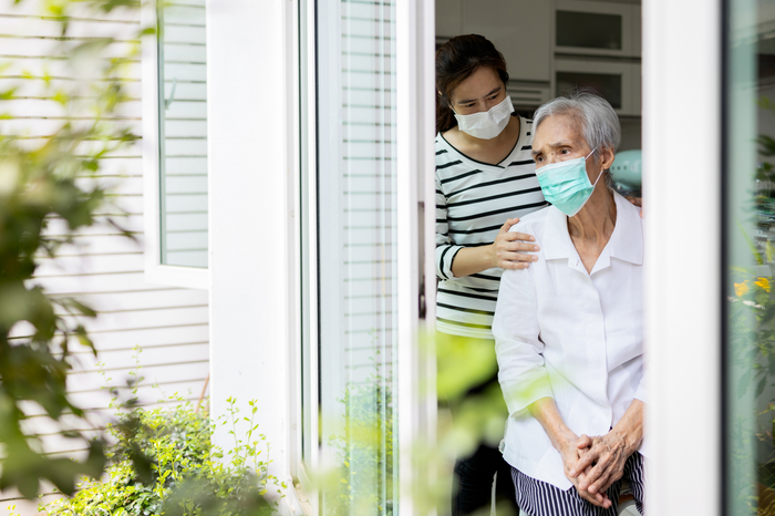 two women looking out of a door. Younger woman is comforting older woman who appears concerned.