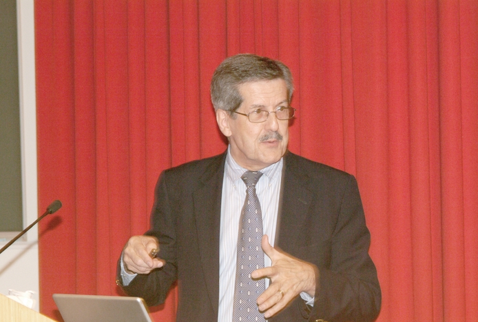A man speaking at a podium in front of a red curtain.