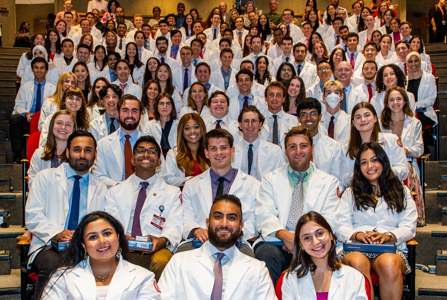Students wearing short white coats sitting in rows of seats in an auditorium.