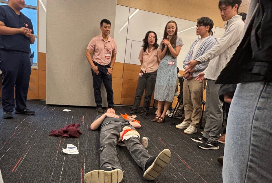 students gather around an actor, lying on the floor, portraying a medical emergency.