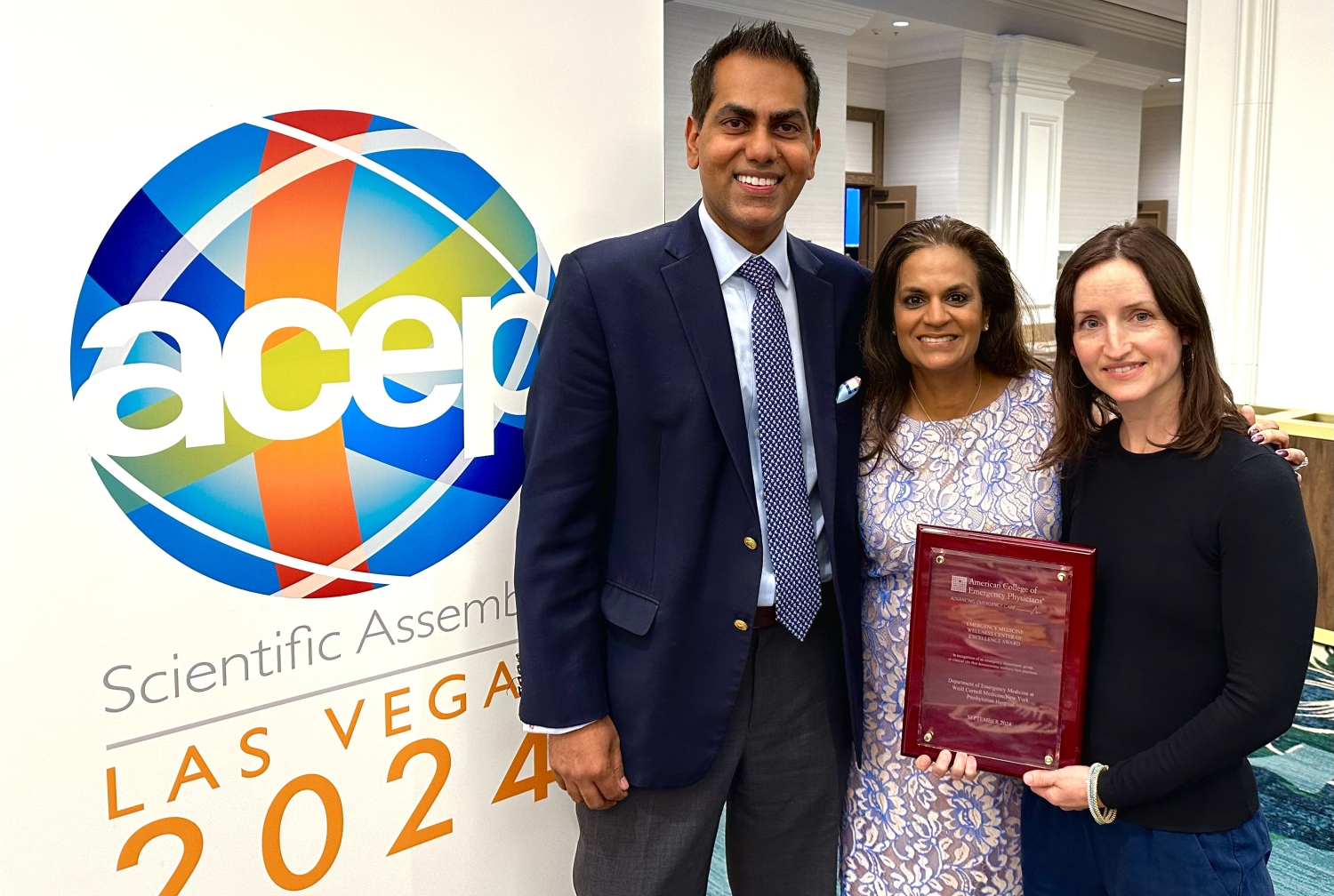 Two women and a man holding an award next to a poster.