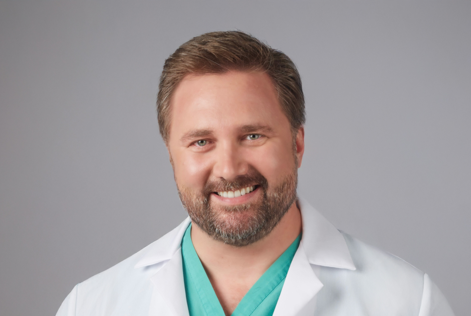 headshot of a physician wearing a white coat and green scrubs