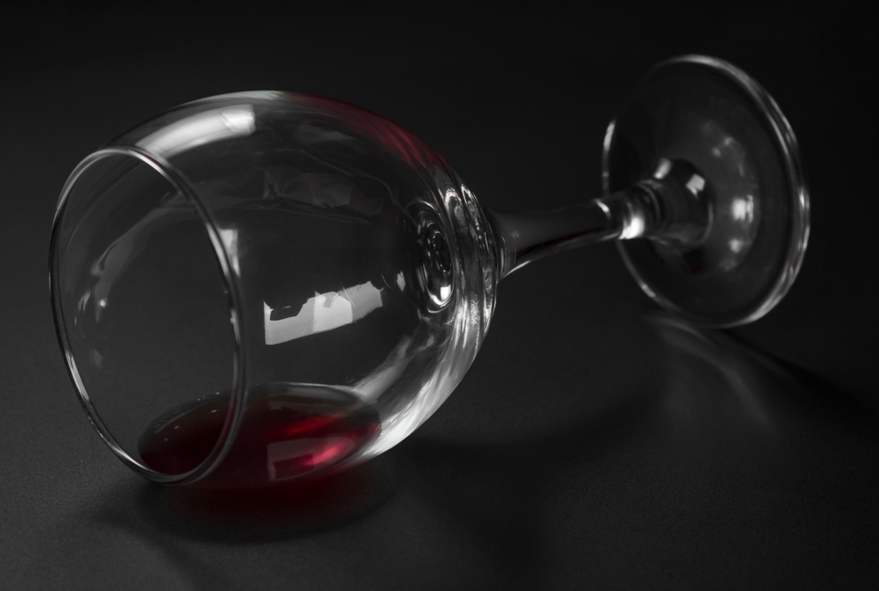 picture of a wine glass with a little red wine in it tipped onto its side