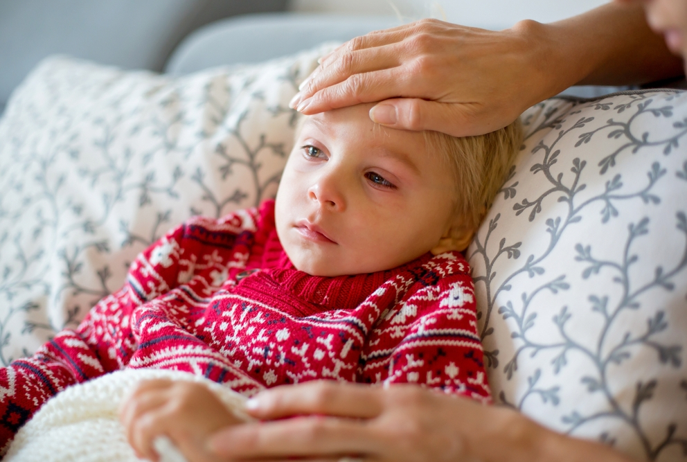 little boy in bed with parents hand on head checking for fever