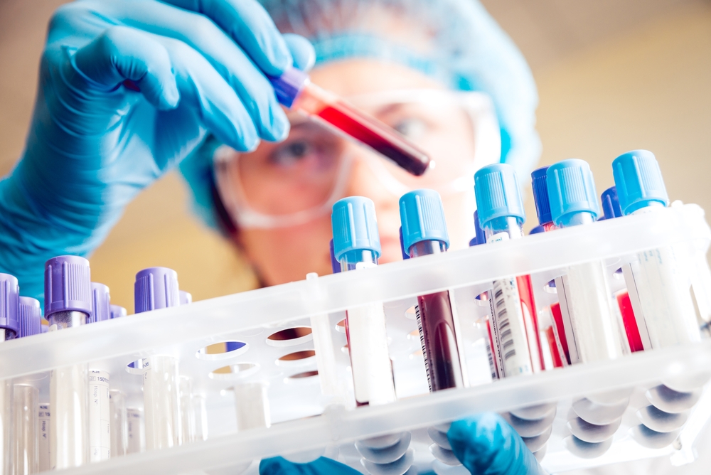researcher holding a vial of blood over a rack of vials
