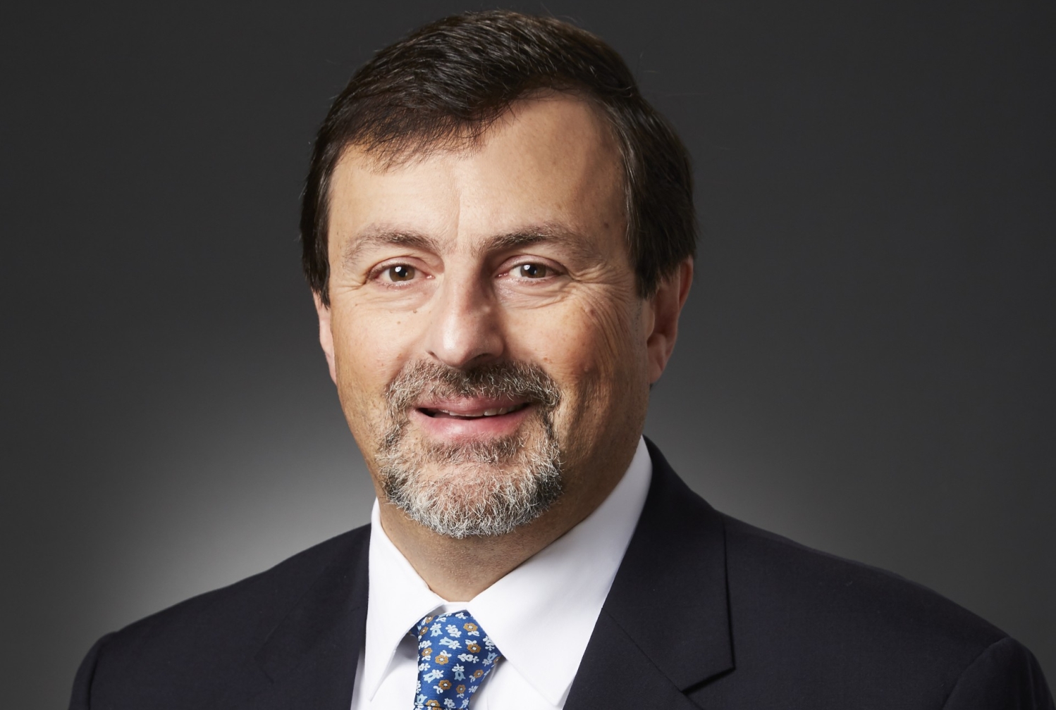 Headshot of a male doctor wearing a suit and blue tie.