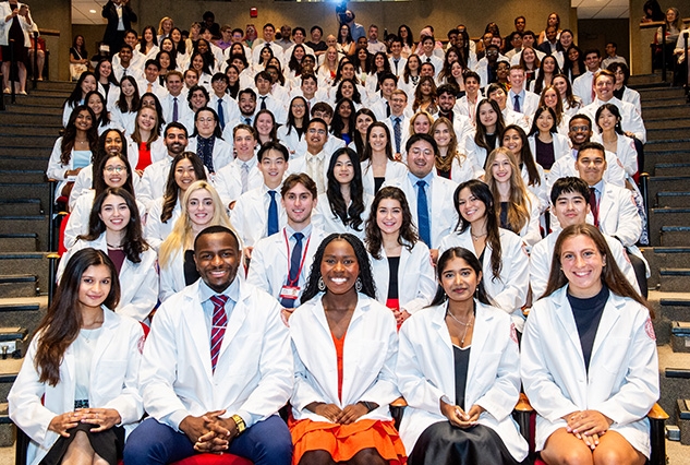 Medical students in white coats sitting in an auditorium.