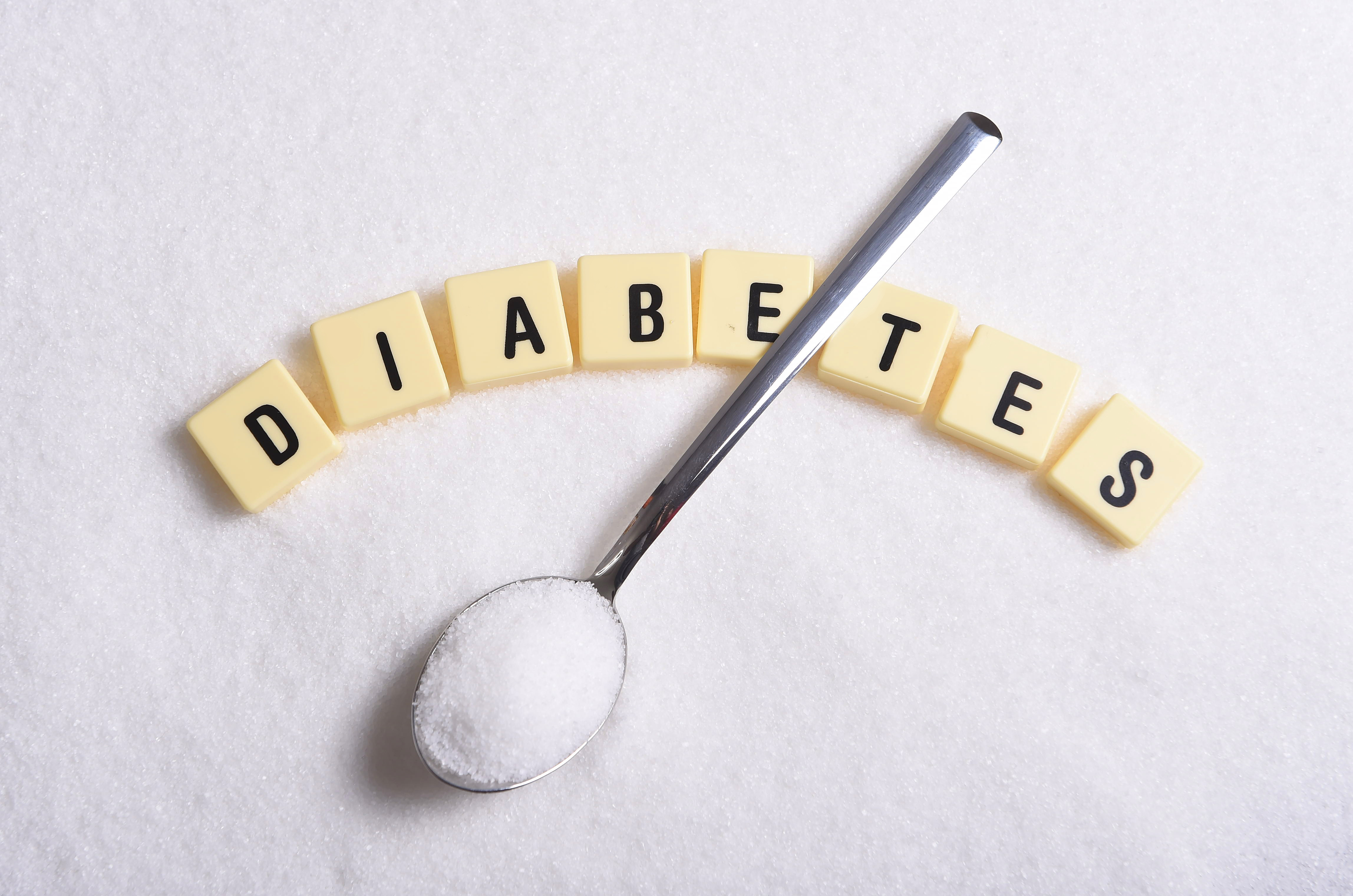 spoon with sugar laying over letter tiles spelling "diabetes"