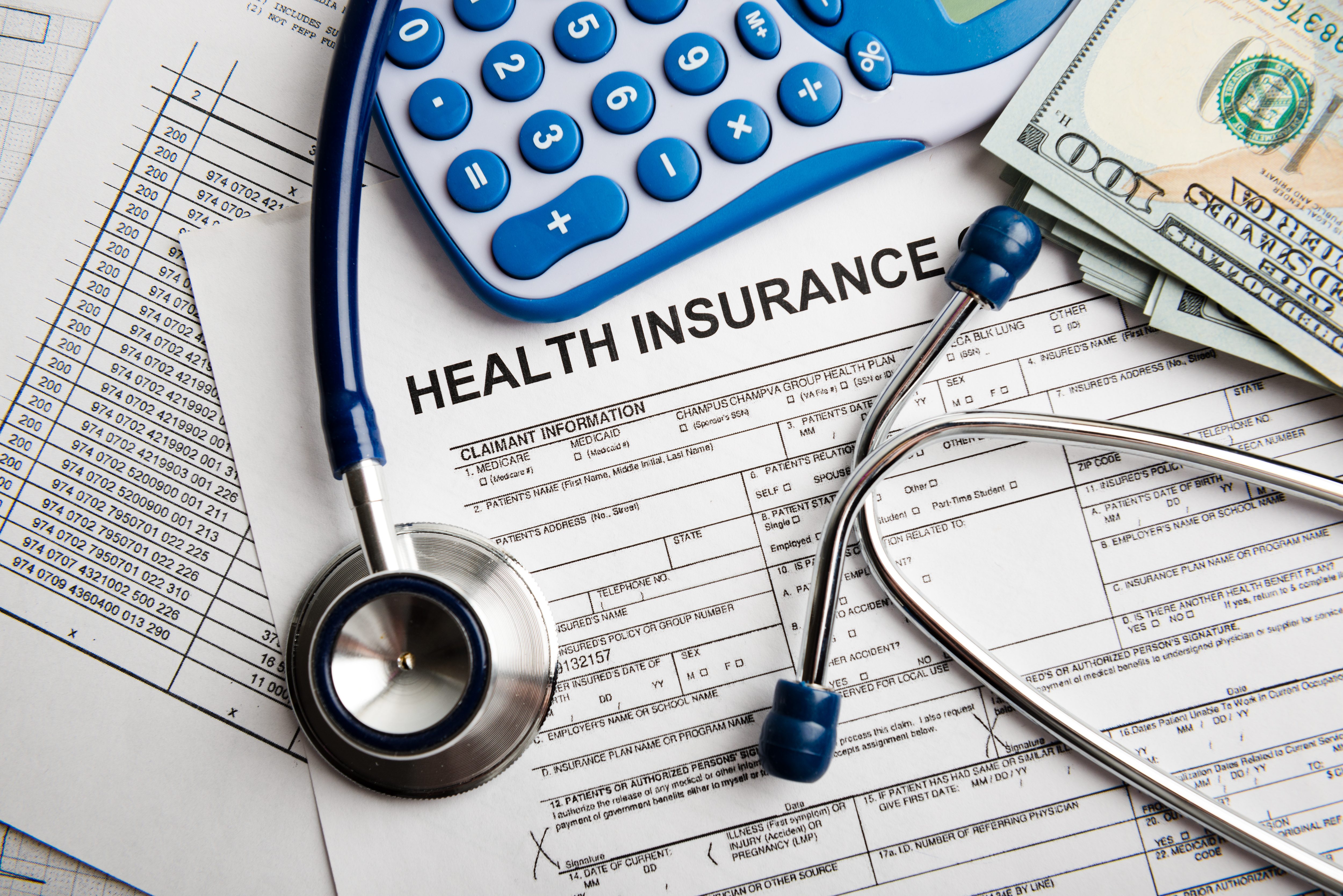 health insurance papers with stethoscope, calculator and money sitting on top.