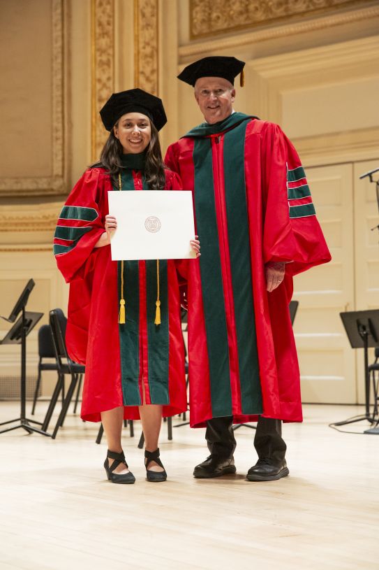 A graduate stands with a school dean on an ornate stage