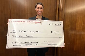 A young Caucasian woman in dark, short hair holding a big check