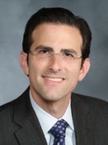a man in glasses and a black suit posing for a headshot
