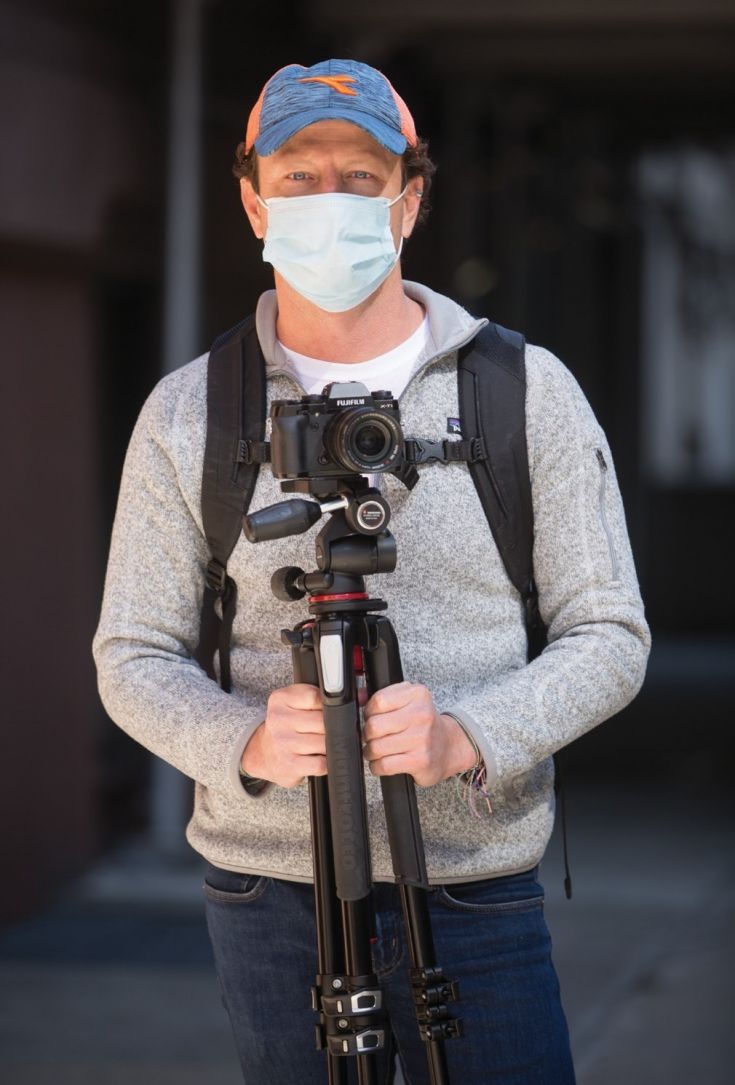 A man wearing a face mask holding a tripod