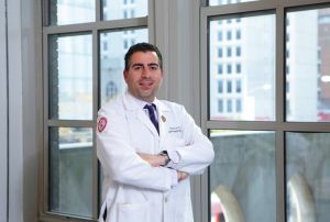 A man in a white coat standing next to a window