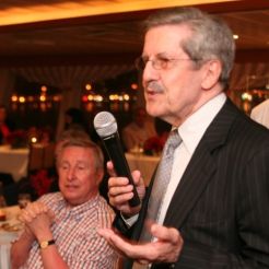 A man using a microphone to speak while another watches on