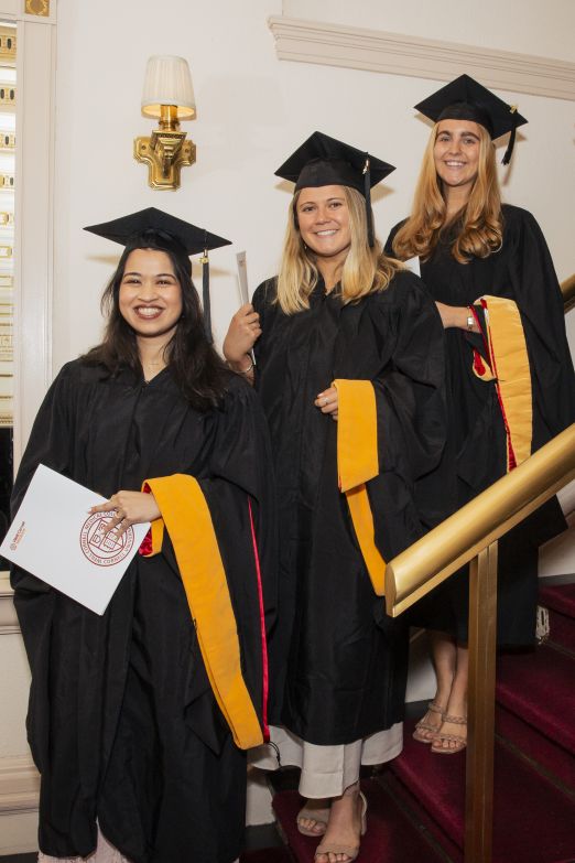 Students wearing black graduation regalia line up on stairs