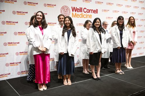 Four students wearing white coats standing in front of four faculty members